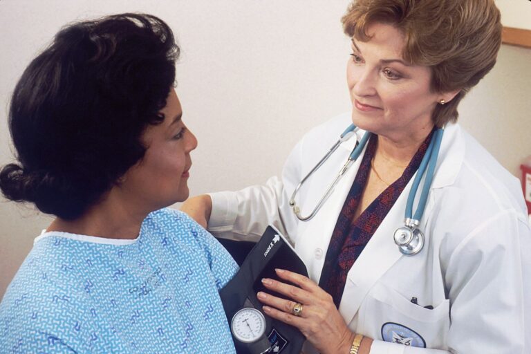 a woman with a stethoscope around her neck, wearing a white lab coat talking to another woman